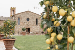 A picturesque view of Belmond Castello di Casole in Tuscany, Italy, featuring a historic stone building and lush lemon trees in the foreground.