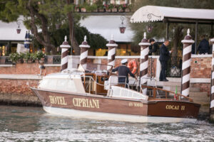 A water taxi labeled "Hotel Cipriani" docked at a pier in Venice, Italy, with a captain preparing to welcome guests.