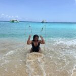 Michelle Norwood joyfully splashing water while seated at the edge of the sea on the beach at Belmond La Samanna in St. Martin.