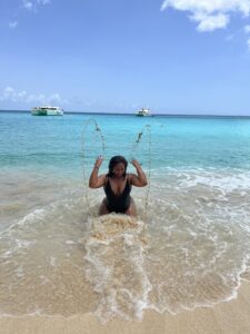 Michelle Norwood joyfully splashing water while seated at the edge of the sea on the beach at Belmond La Samanna in St. Martin.