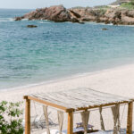 A serene beach cabana at Four Seasons Resort Punta Mita, overlooking a calm sea with rocky outcrops in the background.