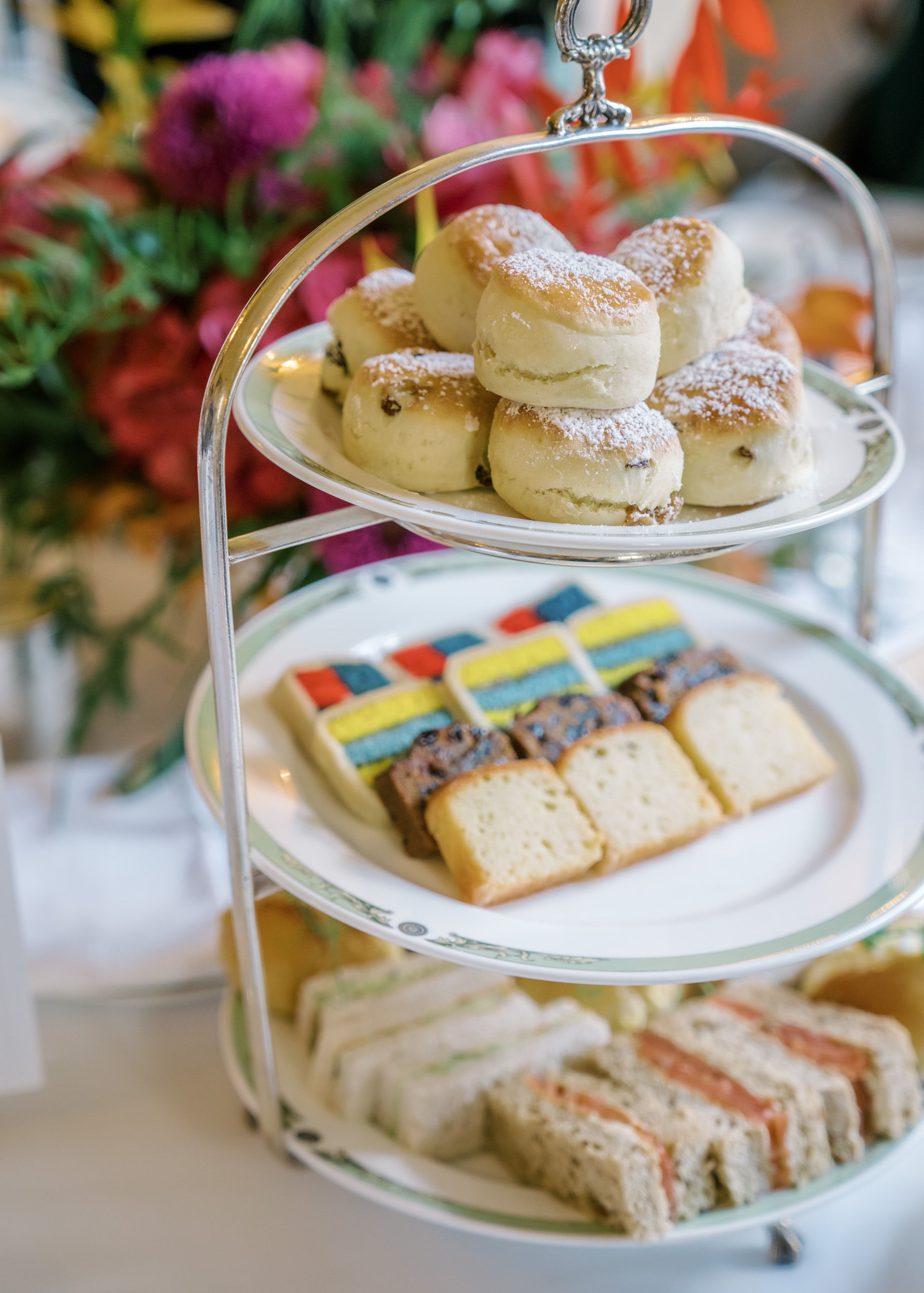 Three-tiered tray with scones, pastries, and tea sandwiches at an elegant high tea party.