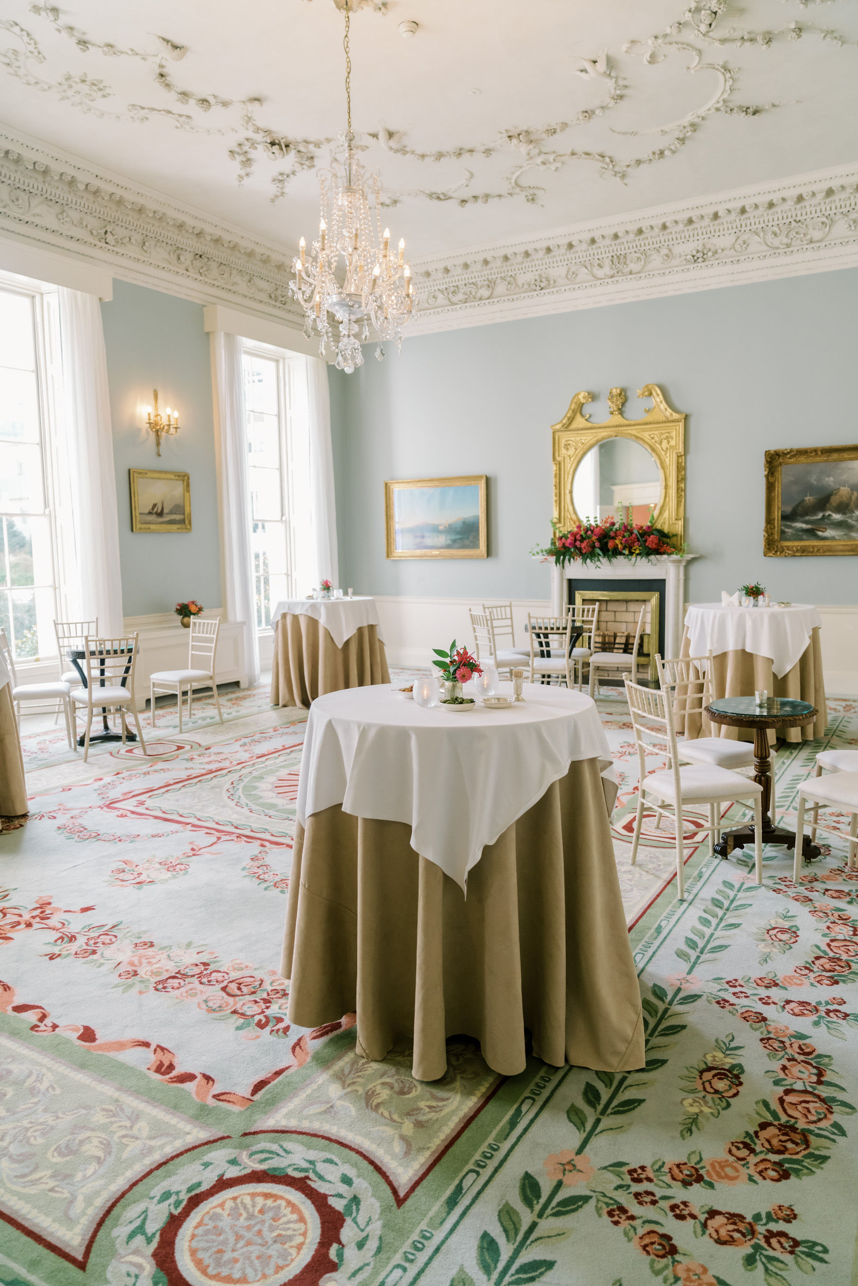 Elegant high tea room with vintage decor, floral centerpieces, and layered table linens.